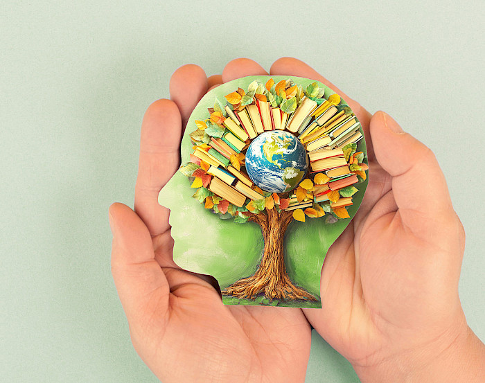 Hände halten einen Kopf bestehend aus einem Baum, der in seiner Krone die Weltkugel und viele Bücher hat