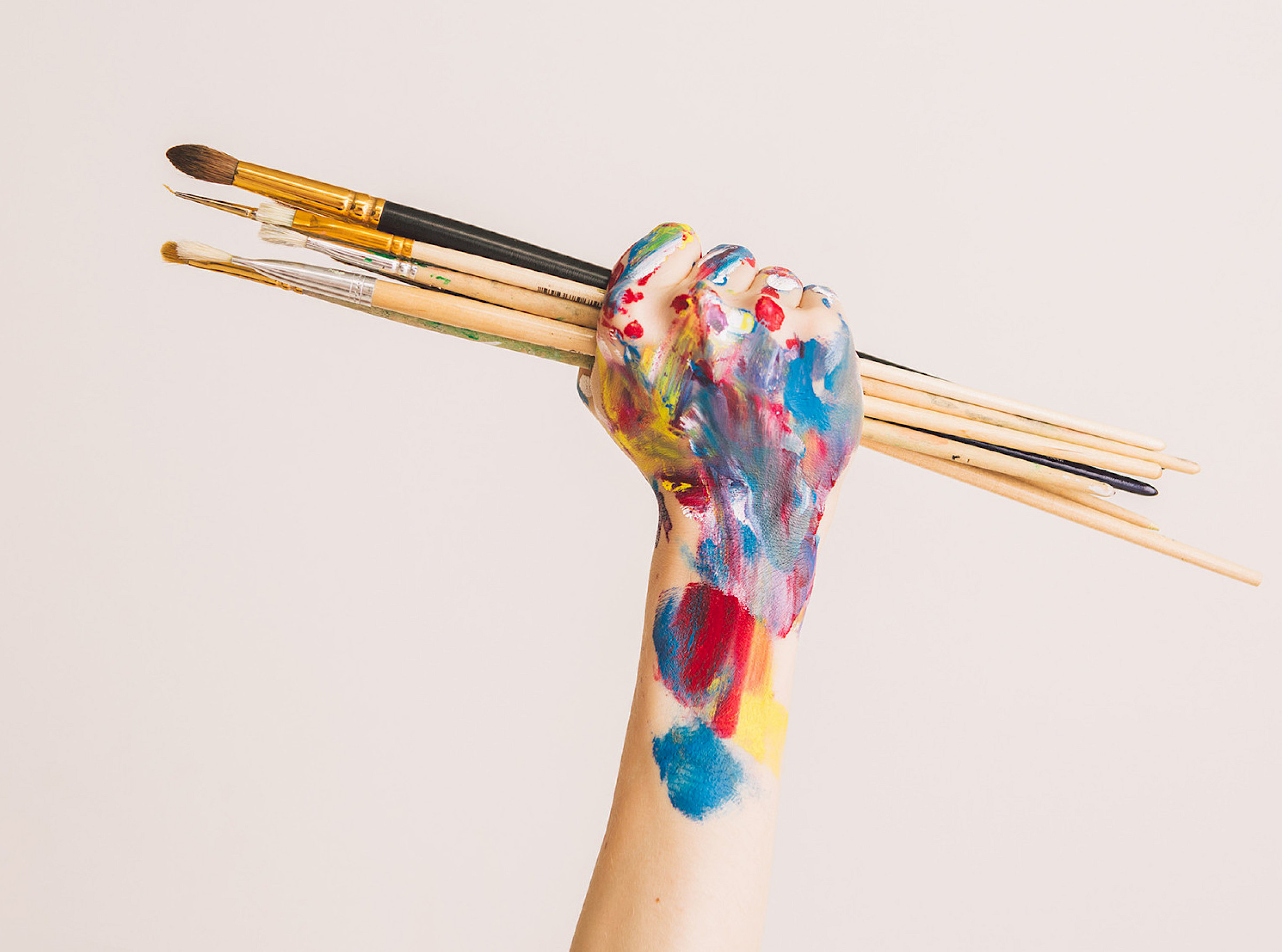 bunt bemalte Hand hält mehrere Malpinsel nach oben
